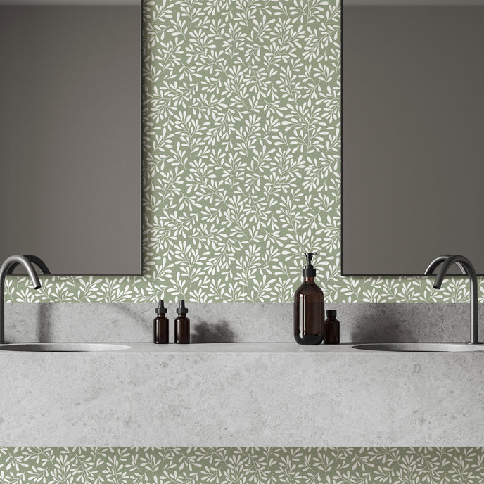 A modern bathroom vanity setup featuring a light grey stone double sink countertop with two dark faucets, two rectangular mirrors, and a sage green botanical wallpaper with a seamless repeat, featuring white leafy sprigs in a simple, elegant pattern.