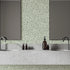 A modern bathroom vanity setup featuring a light grey stone double sink countertop with two dark faucets, two rectangular mirrors, and a sage green botanical wallpaper with a seamless repeat, featuring white leafy sprigs in a simple, elegant pattern.