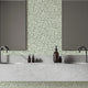 A modern bathroom vanity setup featuring a light grey stone double sink countertop with two dark faucets, two rectangular mirrors, and a sage green botanical wallpaper with a seamless repeat, featuring white leafy sprigs in a simple, elegant pattern.