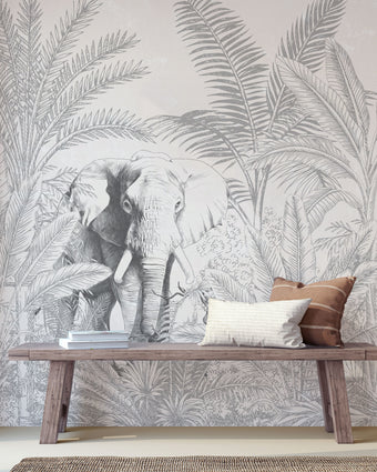 Hand-drawn tropical mural featuring an elephant surrounded by palm trees and dense botanical foliage in soft grey tones. Placed on a wall in a walkway, with a wooden bench in front on the mural.