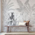 Hand-drawn tropical mural featuring an elephant surrounded by palm trees and dense botanical foliage in soft grey tones. Placed on a wall in a walkway, with a wooden bench in front on the mural.