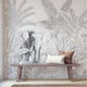Hand-drawn tropical mural featuring an elephant surrounded by palm trees and dense botanical foliage in soft grey tones. Placed on a wall in a walkway, with a wooden bench in front on the mural.