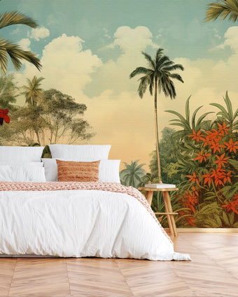 Vintage tropical mural with palm trees, lush green foliage and red orange flowers beneath a soft blue sky, displayed on the wall behind a neatly made bed with white linens and a orange throw blanket, set in a bedroom with wooden flooring.