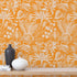 Apricot colour wallpaper with white floral pattern, wooden shelf with decor items.