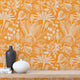 Apricot colour wallpaper with white floral pattern, wooden shelf with decor items.