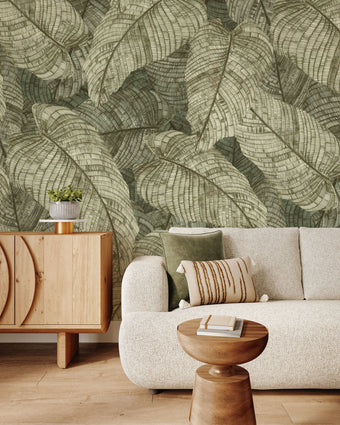 In a seating room there is a vintage botanical wallpaper featuring overlapping fern leaves in soft sage and olive green tones, creating a richly textured nature inspired pattern. 