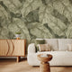 In a seating room there is a vintage botanical wallpaper featuring overlapping fern leaves in soft sage and olive green tones, creating a richly textured nature inspired pattern. 