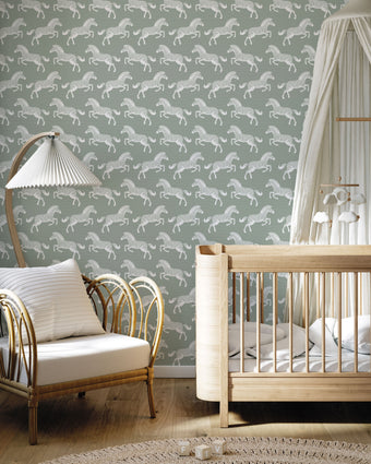 A styled nursery interior with a soft sage green wallpaper featuring a repeating pattern of detailed white zebras. With a light wood crib with white bedding and a white canopy, an armchair with a striped pillow, and a floor lamp near a window.