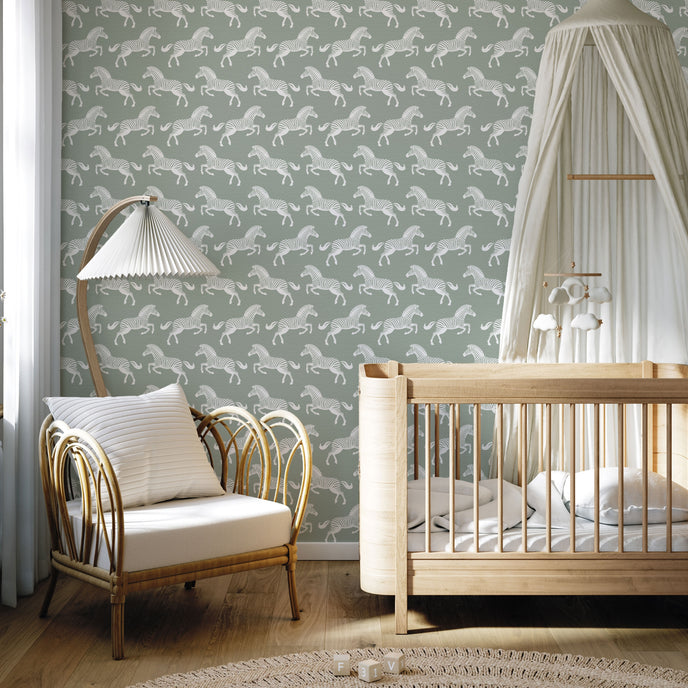 A styled nursery interior with a soft sage green wallpaper featuring a repeating pattern of detailed white zebras. With a light wood crib with white bedding and a white canopy, an armchair with a striped pillow, and a floor lamp near a window.