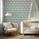 A styled nursery interior with a soft sage green wallpaper featuring a repeating pattern of detailed white zebras. With a light wood crib with white bedding and a white canopy, an armchair with a striped pillow, and a floor lamp near a window.