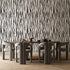 A dining set featuring a rectangular wooden table and six curved grey chairs, set against a bold black and white vertical zebra stripe wallpaper with a seamless repeat, featuring flowing black stripes on a white background in a bold animal inspired pattern, and light wood herringbone flooring.

